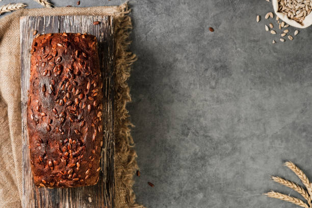 Homemade rectangular wheat and rye bread with seeds, top view. Freshly baked naturally fermented bread lies on a wooden board, a gray table with space for text