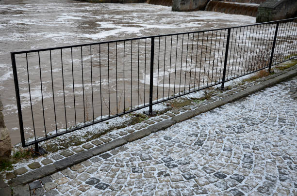 istock Waterfront with a ramp for cyclists and skaters covered with snow dusting. flooded river with waves and dirty water. view of a metal black railing over the river 1364341998