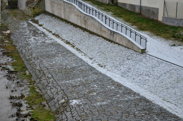 Waterfront with a ramp for cyclists and skaters covered with snow dusting. flooded river with waves and dirty water. view of a metal black railing over the river
