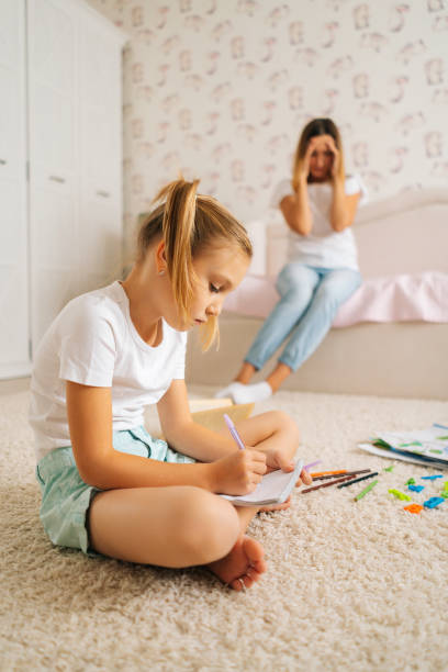 scatto verticale della bambina primaria che scrive i compiti in copybook seduto sul pavimento con il laptop per l'istruzione a distanza online a casa. - elementary age focus on foreground indoors studio shot foto e immagini stock