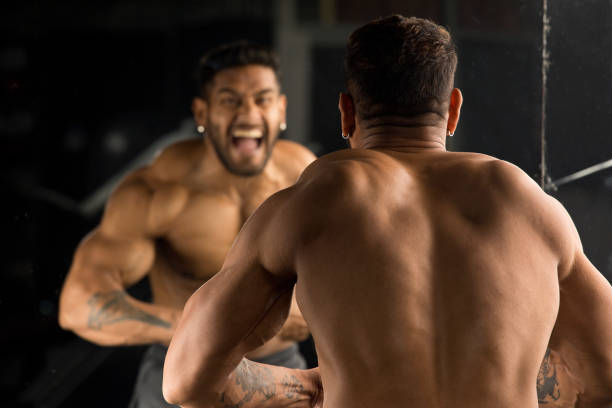 Muscular man flexing muscles in front of mirror Shirtless tattooed muscular man flexing muscles in front of mirror at gym arm tattoo ideas for men pictures stock pictures, royalty-free photos & images