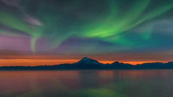 Beautiful Alaskan landscape at sunset of Mount Redoubt volcano and mountain range on the Cook Inlet with the Northern Lights in the sky and reflections in the water