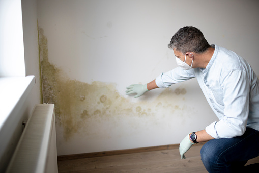 Man with mouth nose mask and blue shirt in front of wall with mold