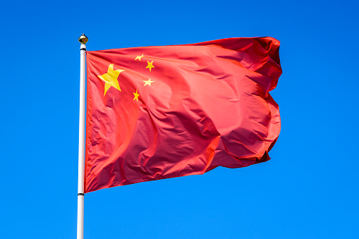 The flag of the People's Republic of China is flying in the wind at full mast against blue sky.