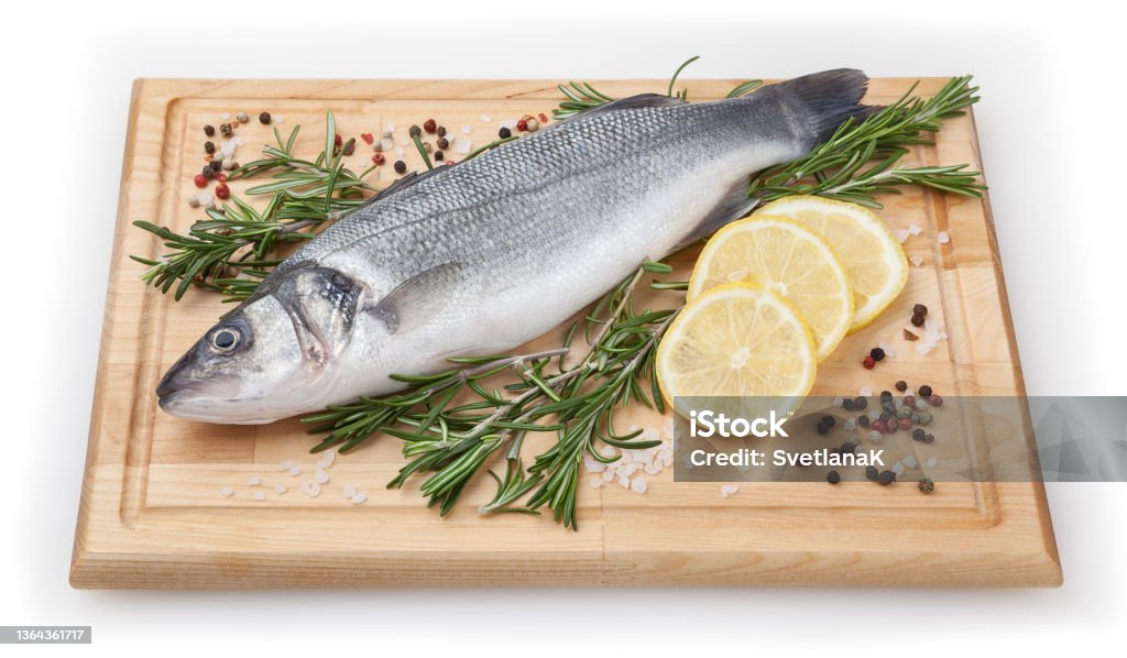 Fresh uncooked seabass with lemon and rosemary on wooden board over white backdground with clipping path Sea Bass Stock Photo