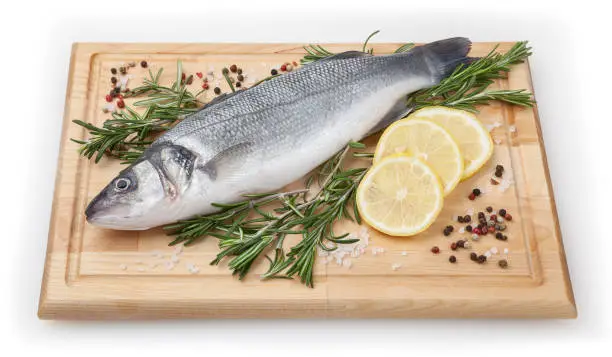 Fresh uncooked seabass with lemon and rosemary on wooden board over white backdground with clipping path