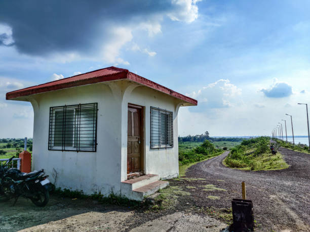 Stock photo of white painted office with red color painted pyramid shape roof top near bennithora water dam. Motorbike parked beside the office,blue sky with dramatic clouds on background at Chittapur foto de archivo de la oficina pintada de blanco con color rojo pintado en forma de pirámide en la azotea cerca de la presa de agua de bennithora. moto estacionada al lado de la oficina, cielo azul con nubes dramáticas de fondo en chittapur