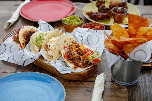 Appetizer served in a plate on restaurant table, Mexican cuisine traditional specialties, folded tortillas with meat and vegetable filling served on wooden board in paper