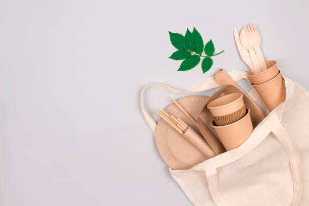 istock Eco-friendly tableware - kraft paper cups and containers in white cotton bag on gray background with copy space for text. Street food take away paper packaging - cups, plates, drinking straws 1364363714