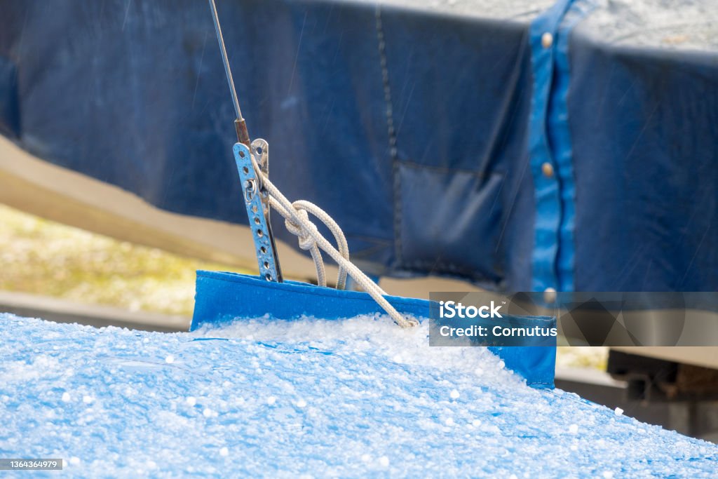 Stag tensioner and tarpaulin with hail A metal stay adjuster and a white attachment line protrude from a blue tarpaulin covered in hail. Adjusting Stock Photo