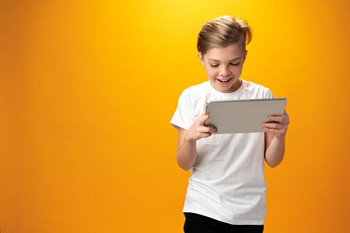 Little boy playing with digital tablet against yellow background, close up