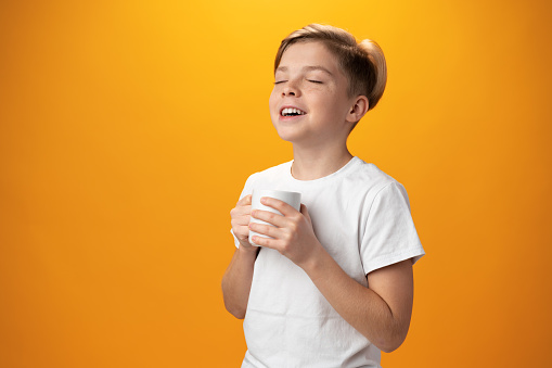 The kid drinking hot cocoa against yellow background, close up