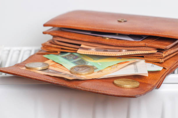 istock Expensive heating costs. Paying bills. Open wallet with Euro money banknotes on heating radiator battery at home 1364367128