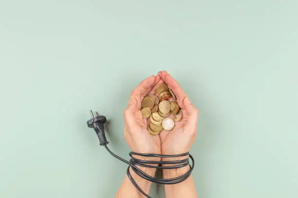 Photo of Female hands tied up with electric power cable cord holding Euro coins. Energy efficiency, power consumption, rising electricity price and expensive energy concept