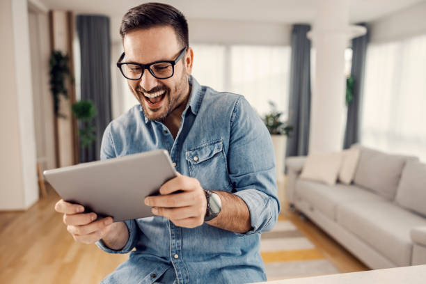 A happy man with using tablet and looking at it at his cozy home. stock photo