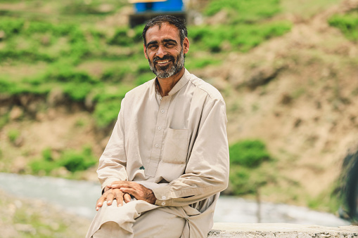 Gilgit, Pakistan - June 09, 2018: Old Pakistani Man with Grey Beard sitting on the Rural Road