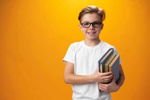 istock Little schoolboy holding a book against yellow background 1364372035