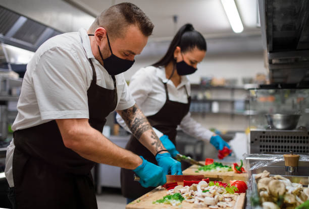 istock Chef and cook with face masks cutting vegetables indoors in restaurant kitchen, coronavirus concept. 1364372301