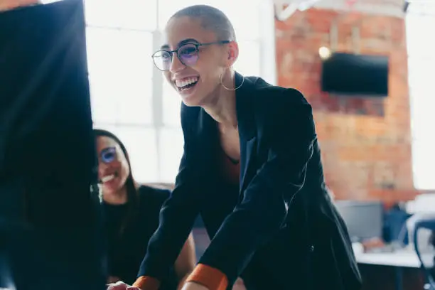 Young businesswoman using a desktop while working with her colleagues. Happy young businesswoman smiling cheerfully while standing next to her colleague at an office desk. Colleagues working together.