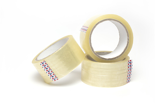 Close up of three rolls of transparent package adhesive tape stacked on top of each other and side by side on white background