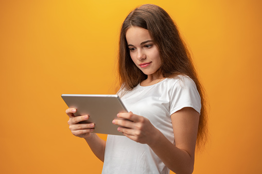 Beautiful teen girl using digital tablet over yellow studio background, close up