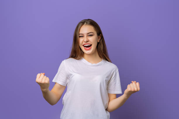 istock Smiling student girl making winner gesture while looking camera, standing against purple background. Celebration concept 1364375706