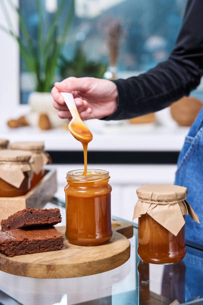 istock a hand with a spoon on which viscous homemade caramel flows into a jar against the background of other packed jars 1364377421