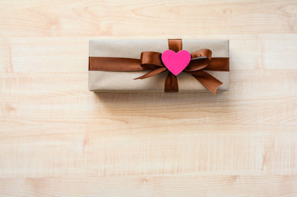 Gift and pink heart on a wooden table. Top view, selective focus on the heart.