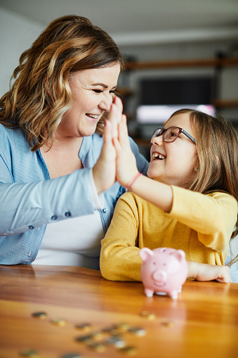 mother and daughter putting coins in a piggy bank at home