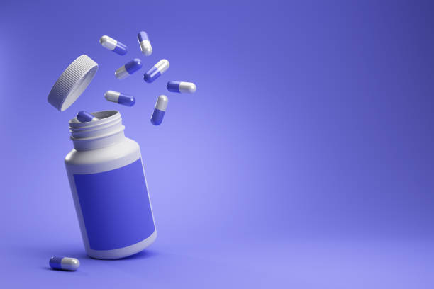 Purple and white capsule pills from white plastic medicine bottle with label on purple background. stock photo