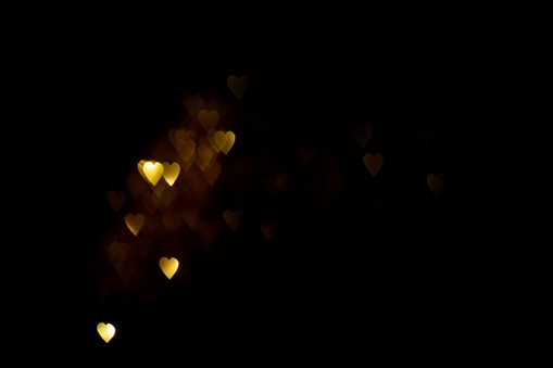 Golden hearts, blurred bokeh lights on black background. Glitter sparkle for celebrate. Overlay for your design