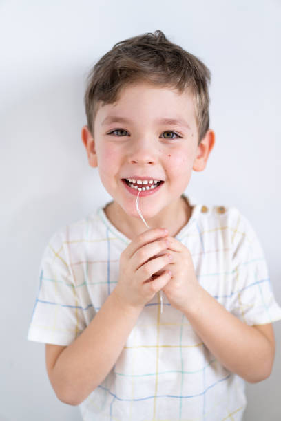 słodki chłopiec ciągnący luźny ząb za pomocą nici dentystycznej. pierwszy ząb mleczny chłopca jest luźny. - children only healthy lifestyle vertical close up zdjęcia i obrazy z banku zdjęć