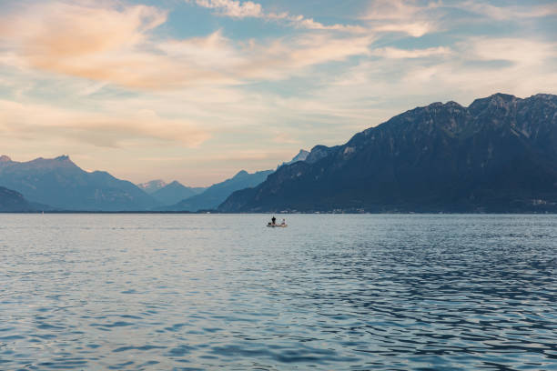 femme et homme flottant dans le bateau contemplant le coucher de soleil pittoresque au-dessus du lac léman et des montagnes des alpes suisses sur fond - lake geneva photos et images de collection