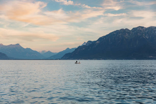 mulher e homem flutuando no barco contemplando o pôr do sol panorâmico acima do lago genebra e montanhas dos alpes suíços ao fundo - lake geneva - fotografias e filmes do acervo