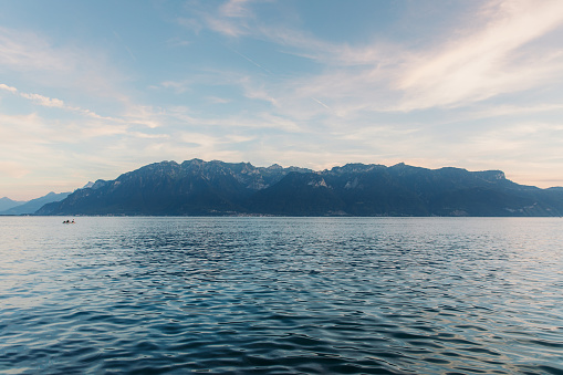 Woman and man floating in the boat contemplating the scenic sunset above lake Geneva and Swiss Alps mountains on background