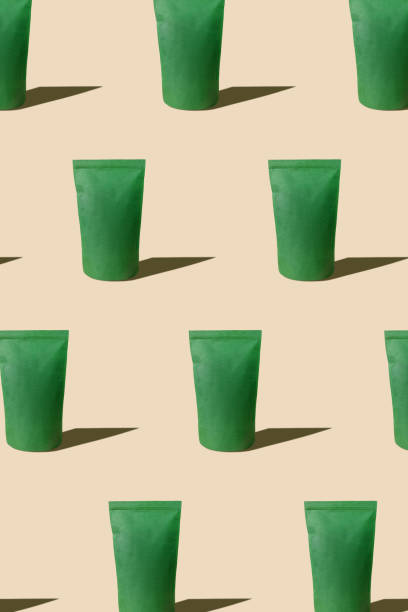 istock Green pouch bag mockup pattern neutral beige background harsh shadows. Blank emerald recycled paper pack coffee beans. 1364385843