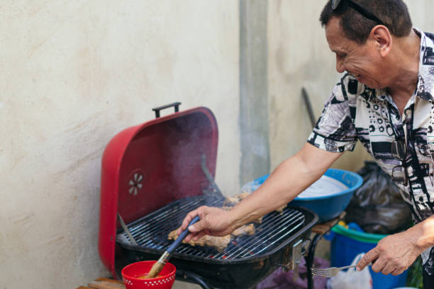 uomo che prepara la carne su un barbecue per il pranzo della sua famiglia nel cortile di casa. - automovil foto e immagini stock