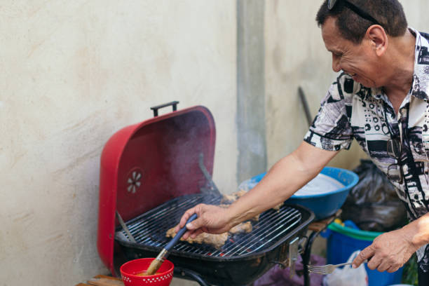 homem preparando carne em uma churrasqueira para o almoço de sua família no quintal. - automovil - fotografias e filmes do acervo