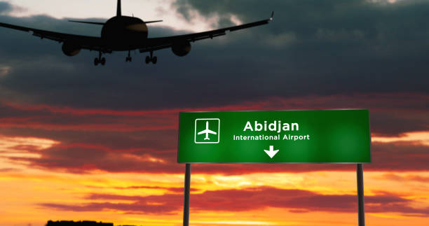 Plane landing in Abidjan Ivory Coast airport with signboard Airplane silhouette landing in Abidjan, Ivory Coast. City arrival with airport direction signboard and sunset in background. Trip and transportation concept 3d illustration. abidjan airport stock pictures, royalty-free photos & images
