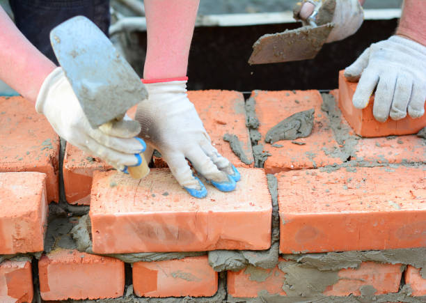 zwei maurer legen ziegel einer ziegelmauer, fundament mit einer maurerkelle und mörtel. eine nahaufnahme eines mauerwerks aus gebrannten tonziegeln. - mason brick bricklayer installing stock-fotos und bilder