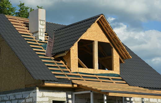A house under construction with a close-up of the roofing construction on the stage of roof framing over a vapor barrier, metal tiles and flashing installation. Roofing Construction.