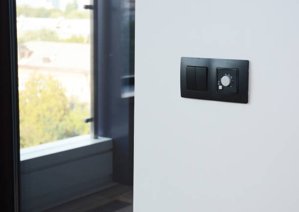 istock A close-up of a modern elegant black light switch and a climate, temperature control panel, the thermostat of a heater installed on a white wall in a room near a window. 1364390705