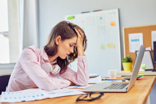 Tired young woman in office having headache working on project stock photo