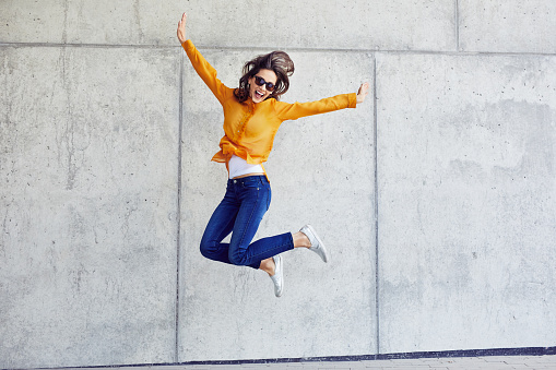 Happy woman jumping against concrete wall in the city