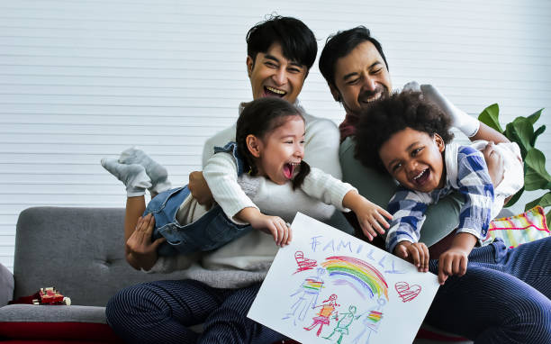 male gay taking care adopted children who are happy diverse little caucasian girl and african boy, playing with fun, drawing family picture, sitting on sofa in living room at home. lgbt, kids concept. - child little boys male caucasian imagens e fotografias de stock