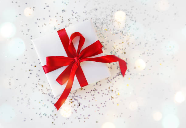 istock Gift box wrapped in white paper with a red bow on festive light background 1364392885