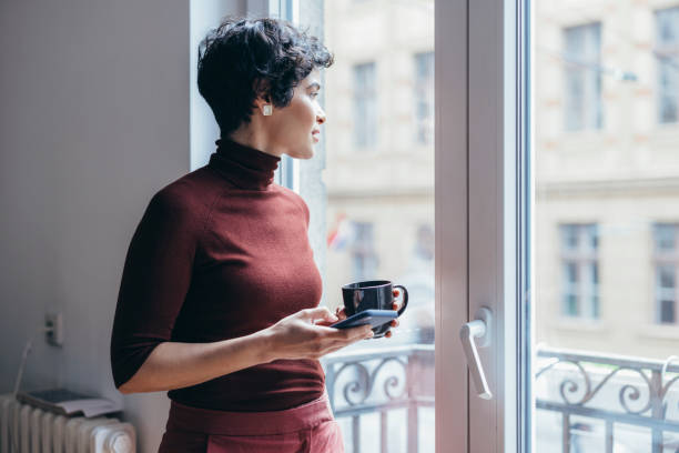 istock A Hardworking Latin-American Female Taking A Break And Looking Through The Window While Drinking Her Coffee And Using Her Smartphone 1364393638