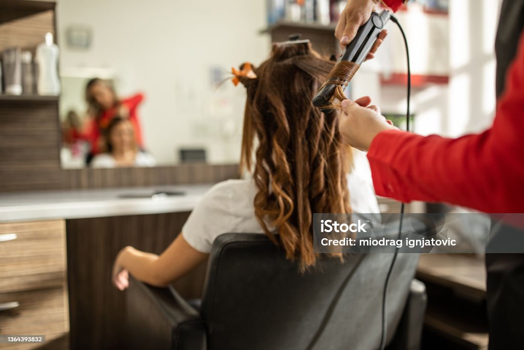 Unrecognizable hairdresser using hair straightener to make curls Unrecognizable professional female hairdresser, making a curly hairstyle, with hair straightener, to her female client, at modern hair salon 30-34 Years Stock Photo