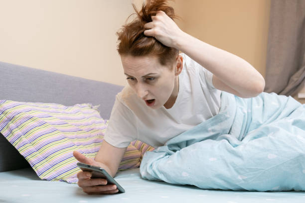 Woman overslept and looks at the time on her smartphone in shock Woman overslept and looks at the time on her smartphone in shock. Middle-aged woman is late due to late awakening. The alarm did not go off on the smartphone. oversleeping stock pictures, royalty-free photos & images