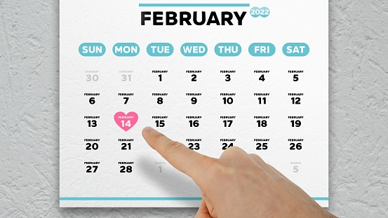 A man points finger to Valentine’s Day on a February page of the wall calendar 2022